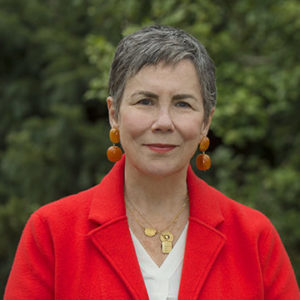 Susan Barry shown wearing a red blazer with wooded backdrop